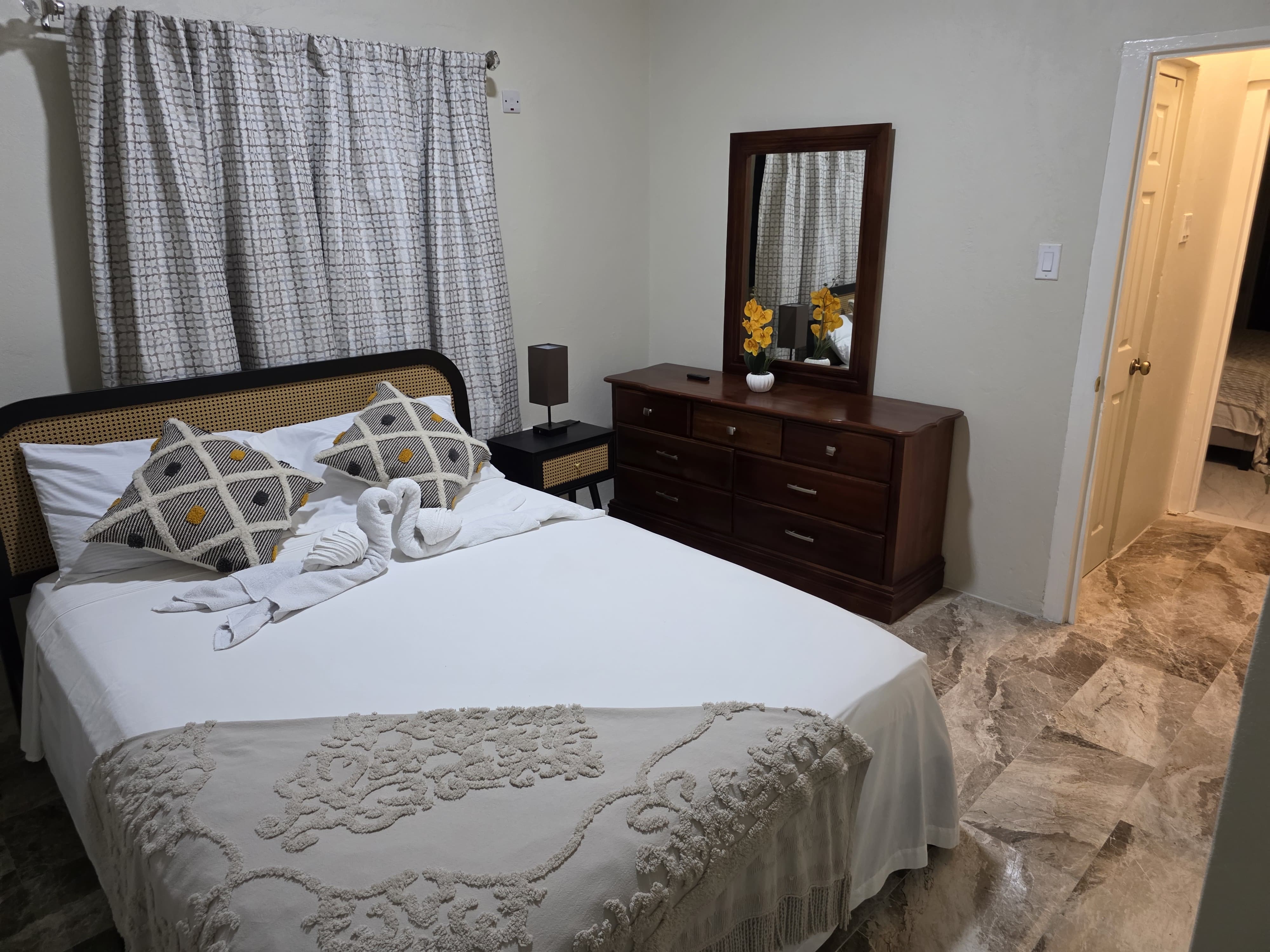 Bright bedroom with a queen bed, wooden dresser and a vase of yellow orchids