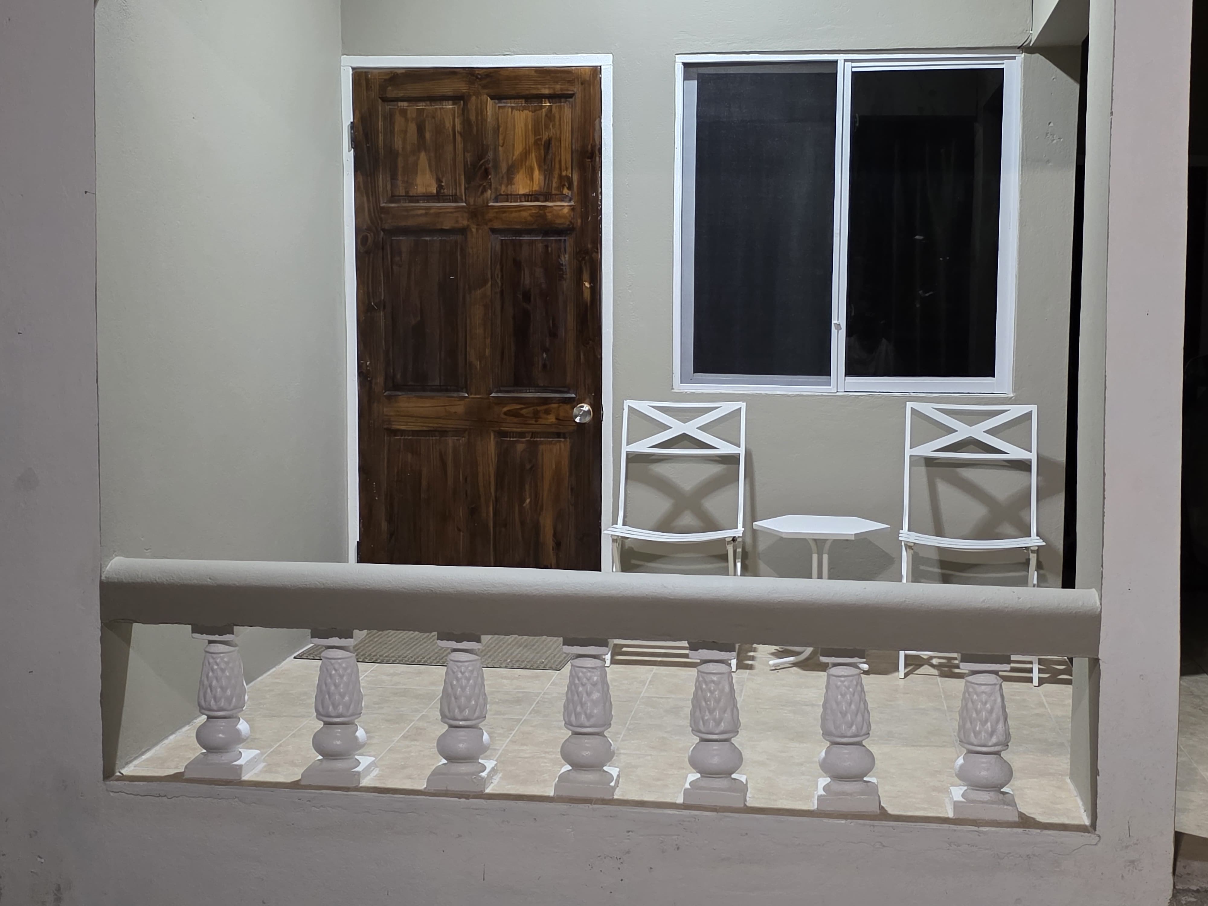 The estate's wooden front door with a balustrade and white bistro chairs in the evening