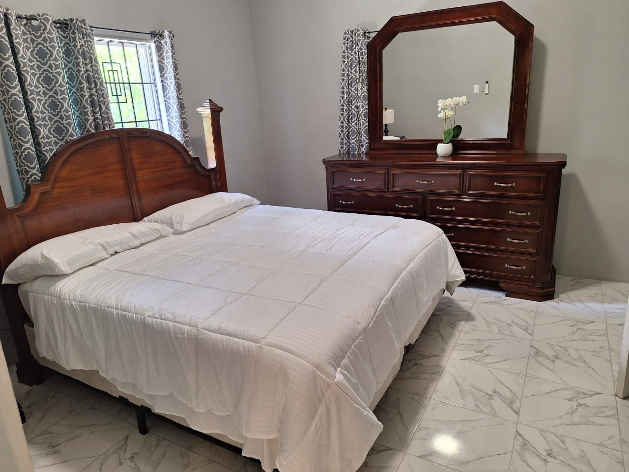 Queen bed with carved wooden headboard, wood dresser with mirror and a single white orchid