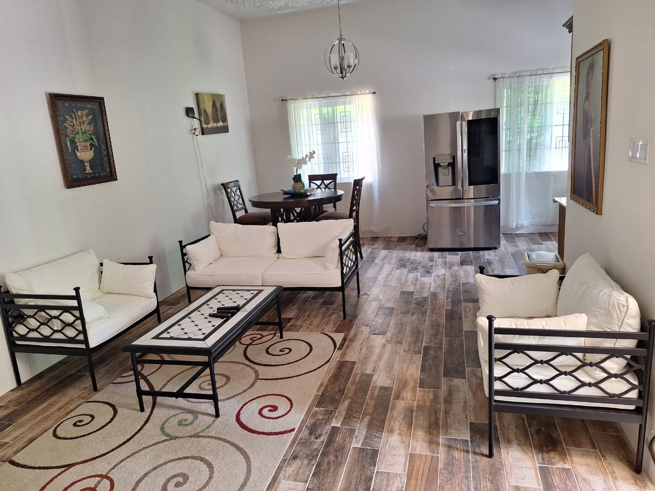 Open living and dining room with white-cushioned sofas, a small chandelier and bright windows